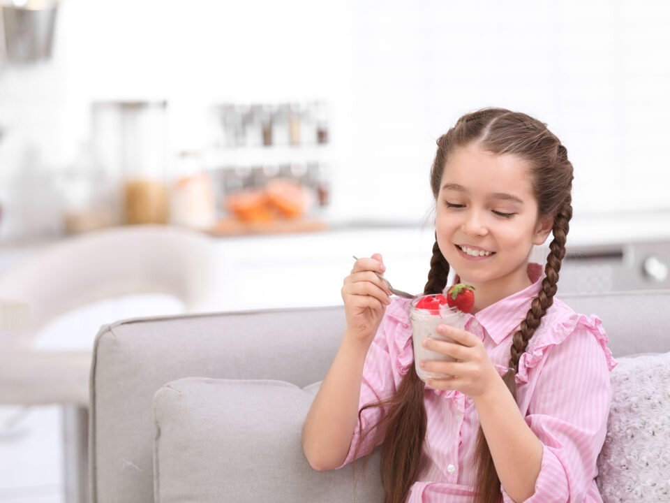 a girl eating yogurt and strawberries on her couch at home