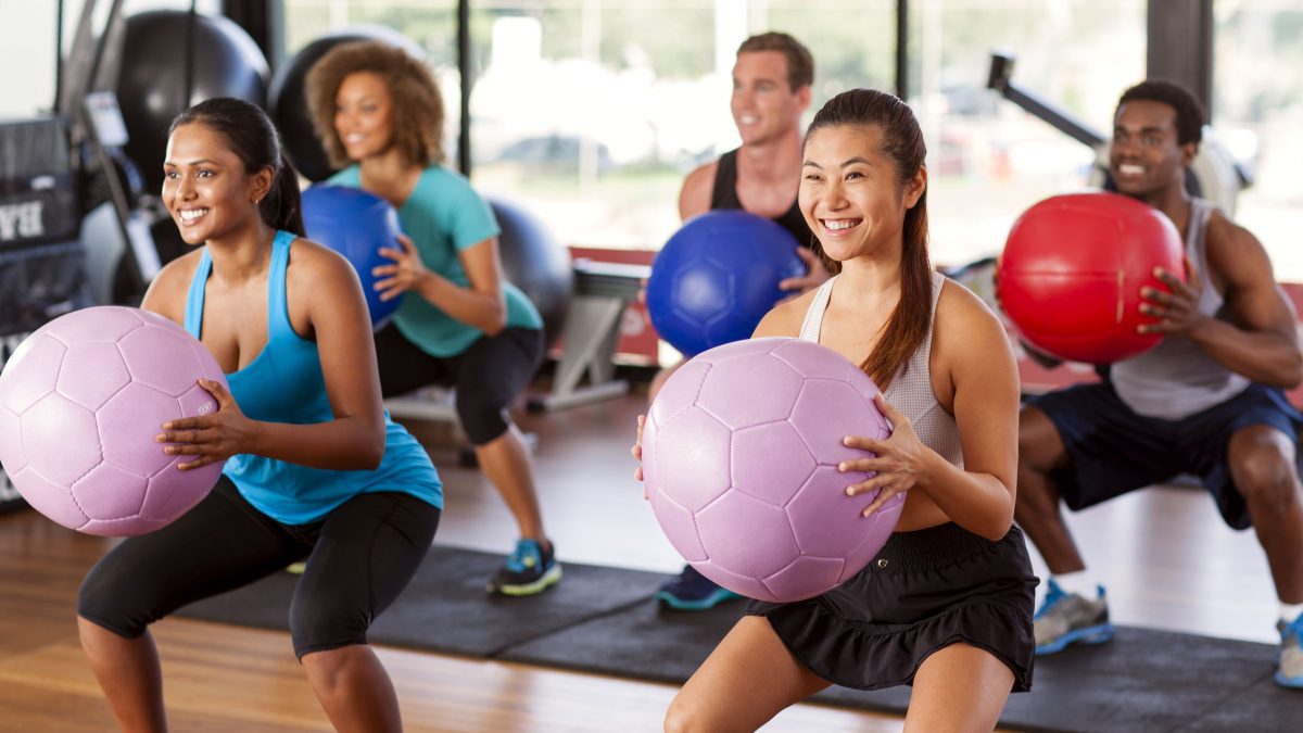 women and men squatting with exercise balls in a group fitness class