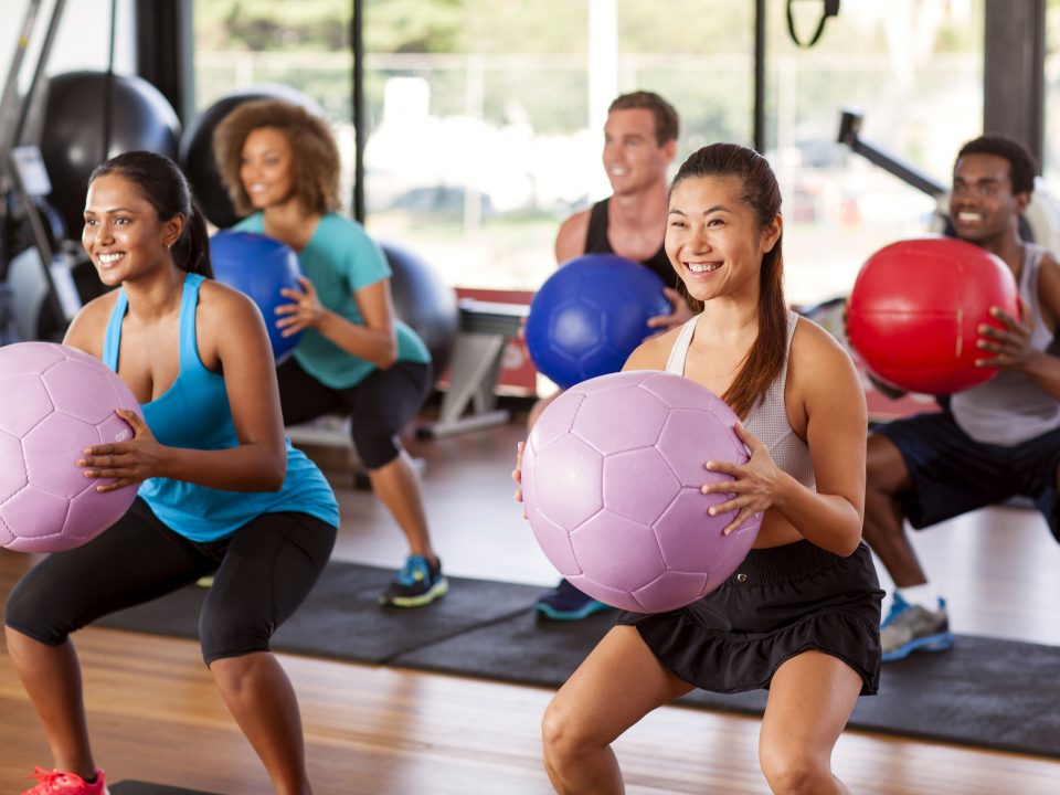 women and men squatting with exercise balls in a group fitness class