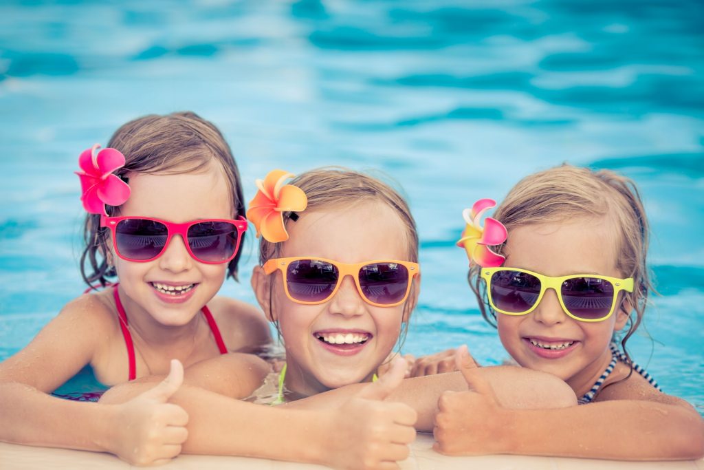 three girls with sunglasses smiling in the pool after a swim lesson