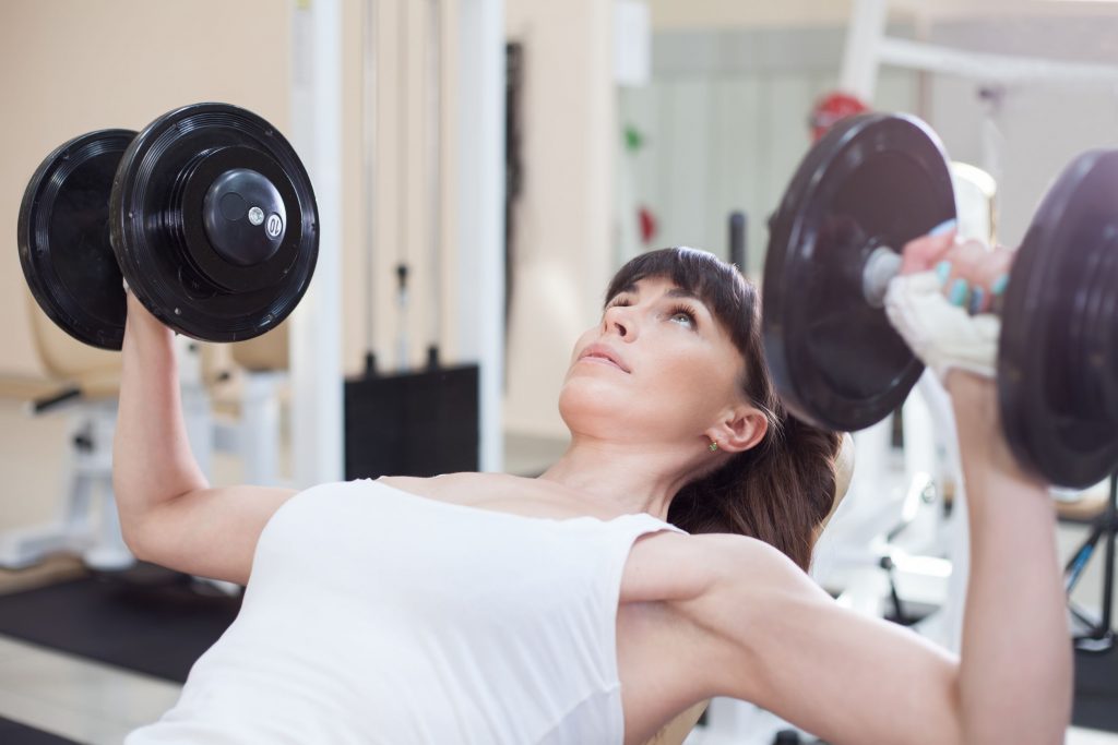 Woman lifting dumbells while seated on a bench at the gym