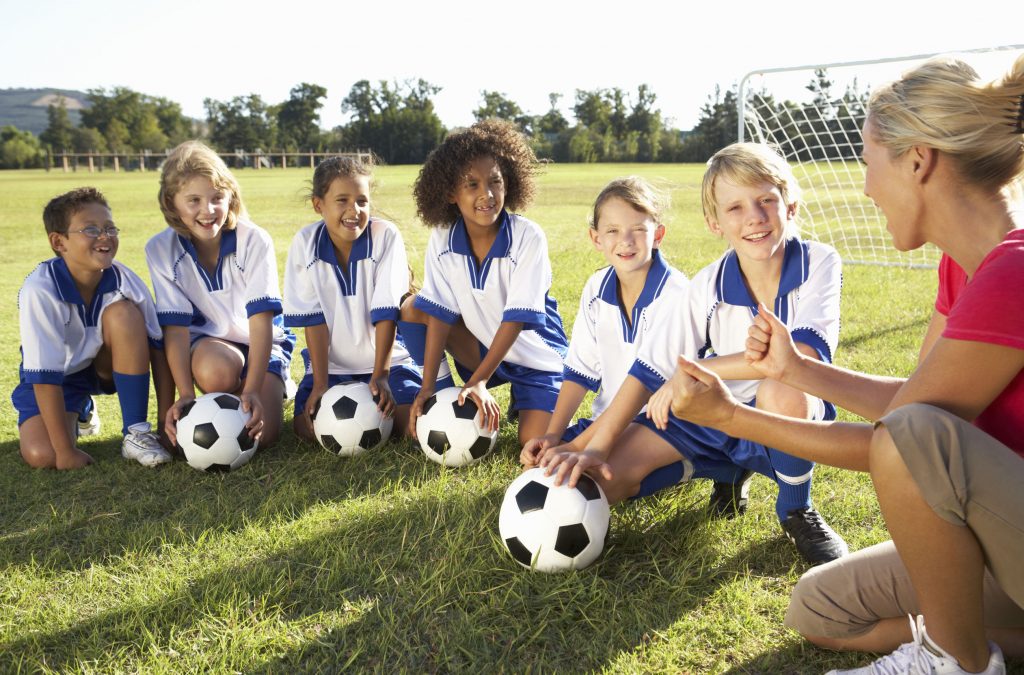 kids’ soccer team with boys and girls surrounding a coach