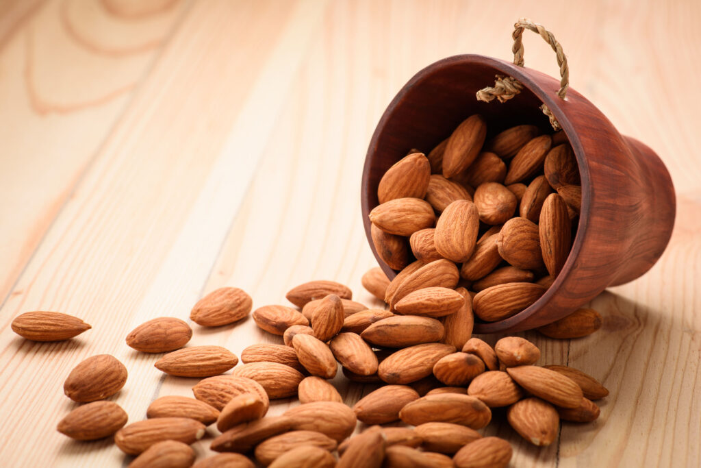 a wooden bowl with almonds spilling out onto a wooden table