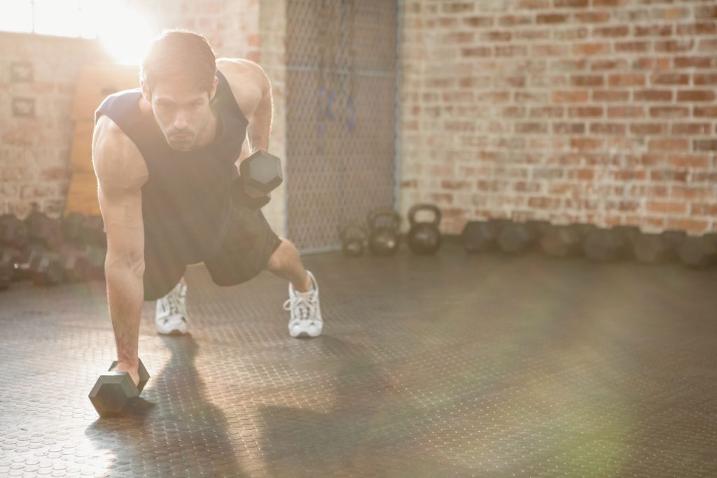 Focused man strength training by lifting dumbbells