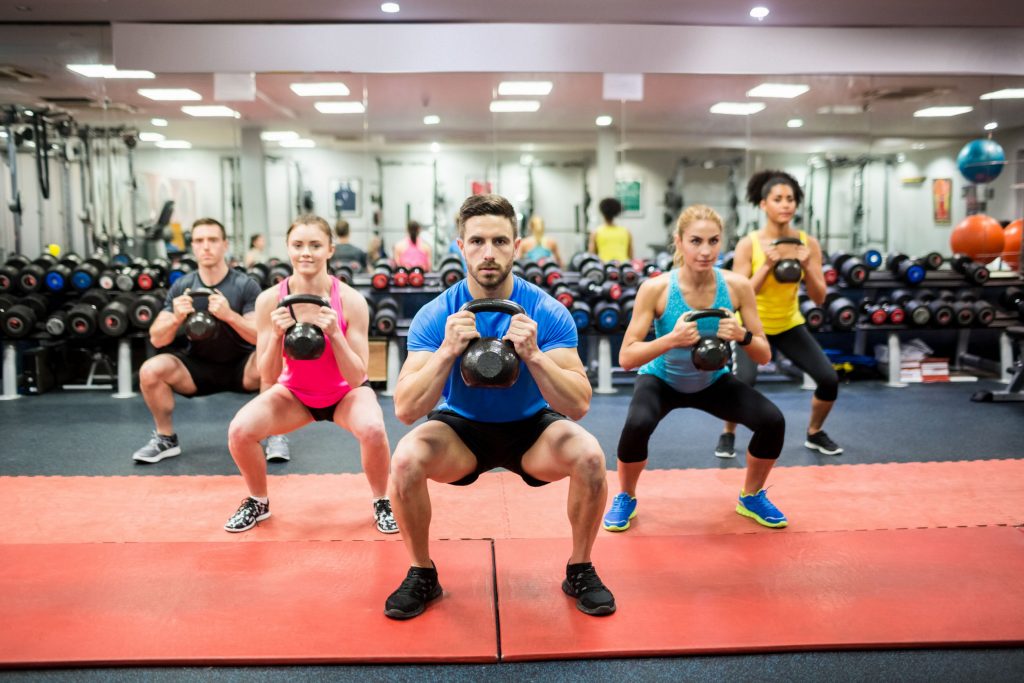 men and women squatting with kettlebells in a group fitness class