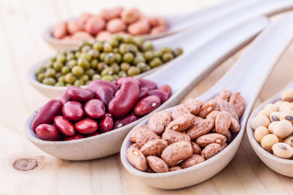 five white spoons holding beans and other legumes