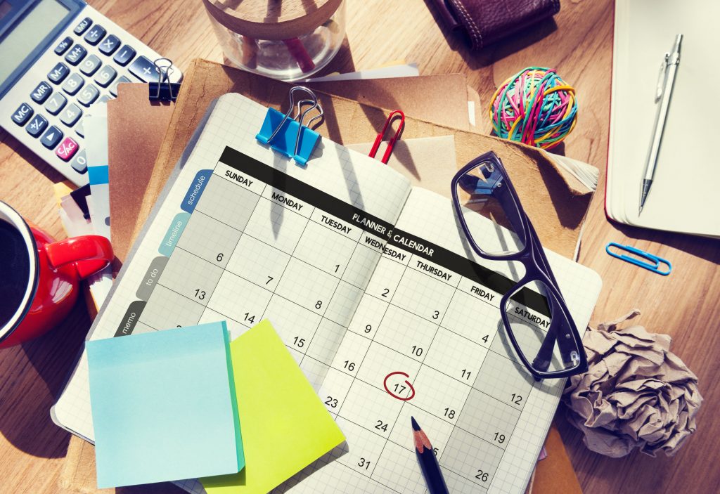 calendar on desk with coffee, rubber band ball, pencil, sticky notes, and paper clips