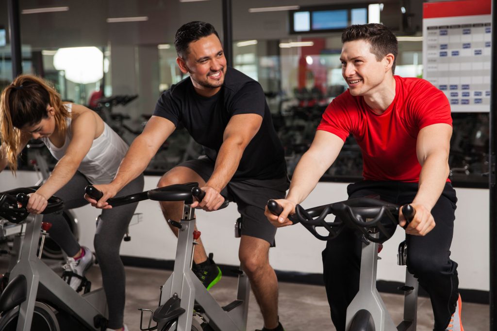 two men smiling and talking while on bikes in a spin class