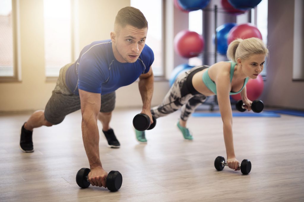 Couple working out together by doing push-ups with dumbbells