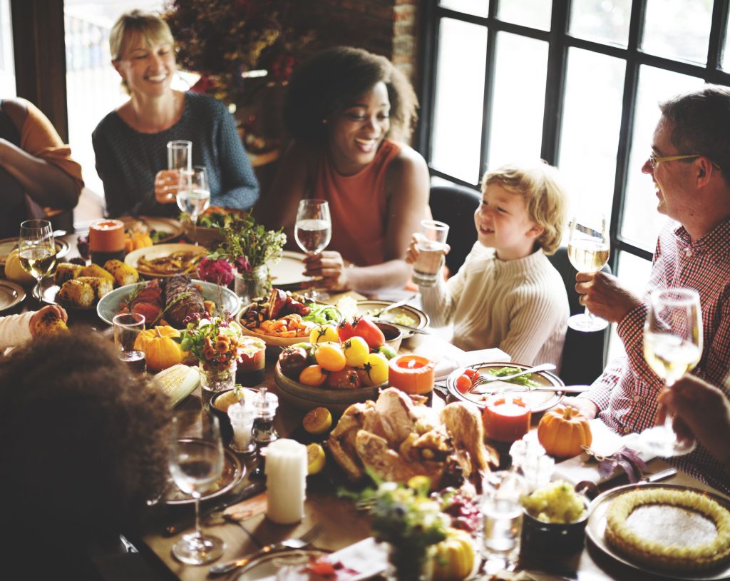 multigenerational family celebrating Thanksgiving with turkey, peppers, corn on the cob, and other foods