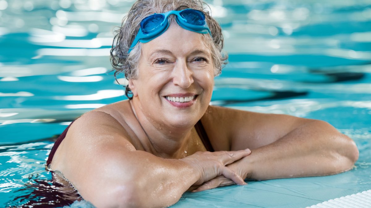 a senior woman smiling while in the pool during an aquatic group fitness class