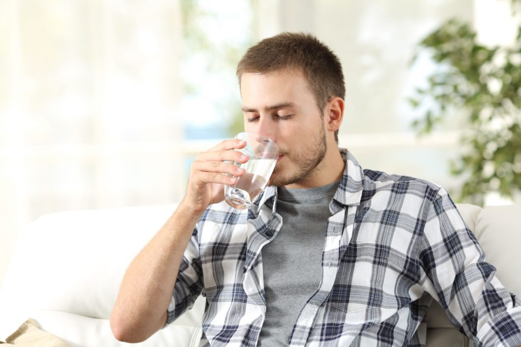 male college student drinking water while sitting on a couch