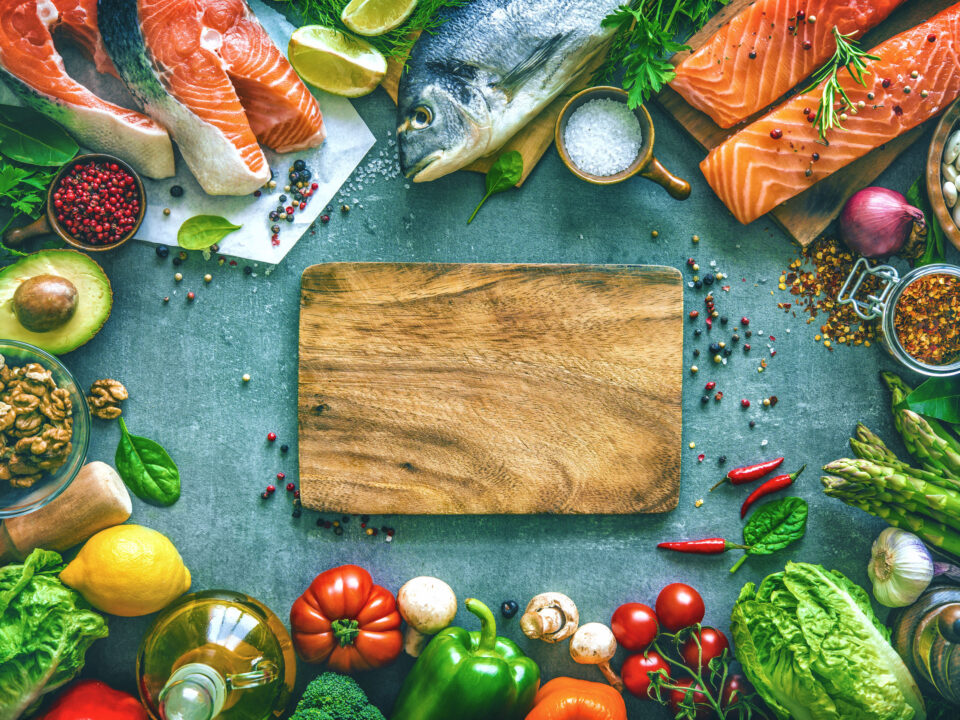 low-cholesterol foods like salmon, avocados, tree nuts, lemons, and red bell peppers on a gray background