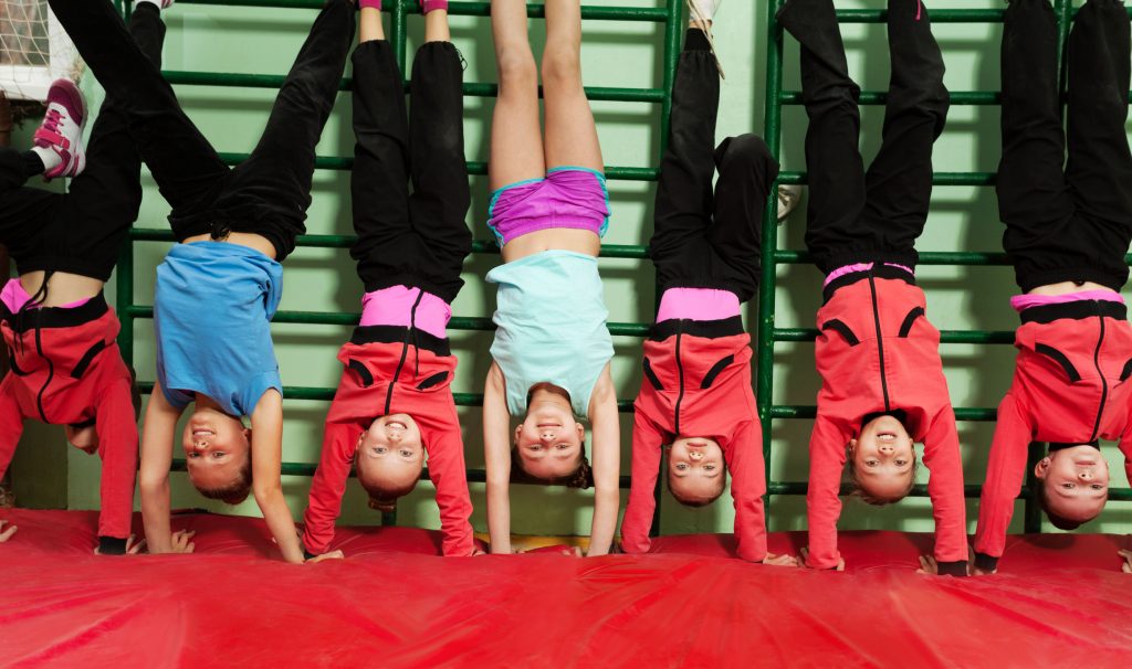 boys and girls doing handstands on a red gym mat