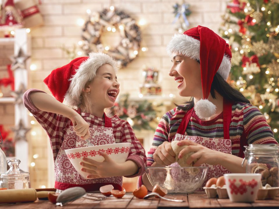 mom and daughter in Santa hats baking together by a Christmas tree