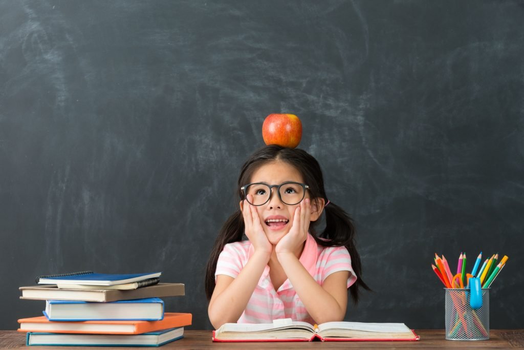 schoolgirl with pigtails and books, balancing an apple on her head in front of a chalkboard