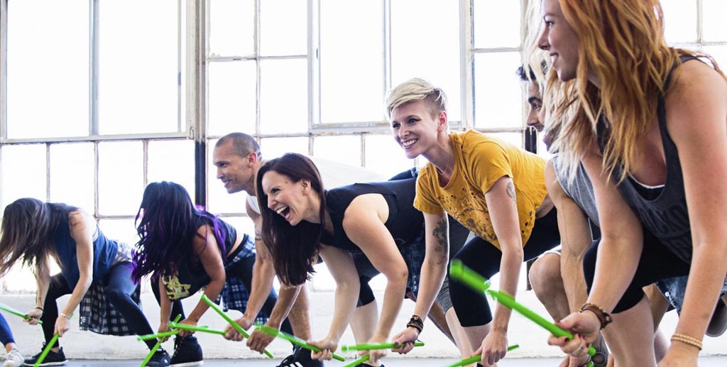 young adults hitting the ground with green drumsticks at a Pound class