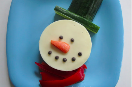 snowman made from a circular sandwich, cucumber slices, red bell peppers, raisins, and a carrot